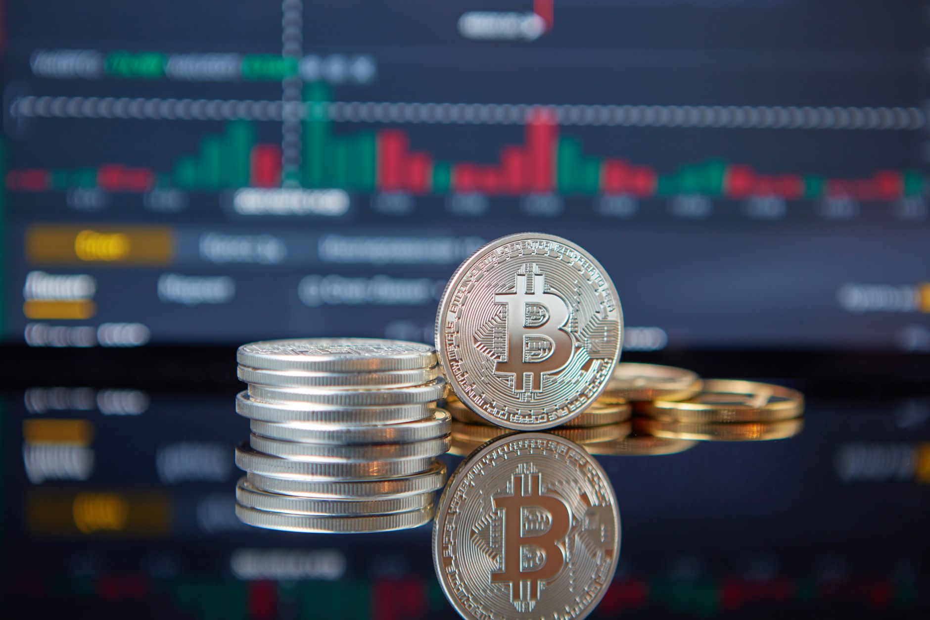 Stack of Bitcoin coins in front of a stock market graph, reflecting cryptocurrency trends.