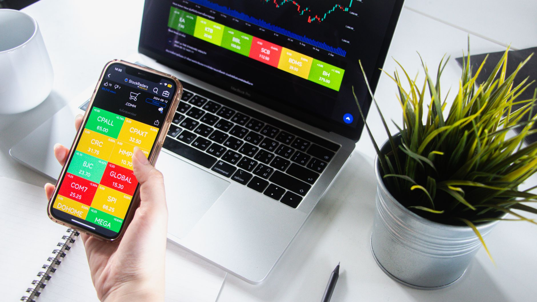 Person analyzing stock market trends on smartphone and laptop.