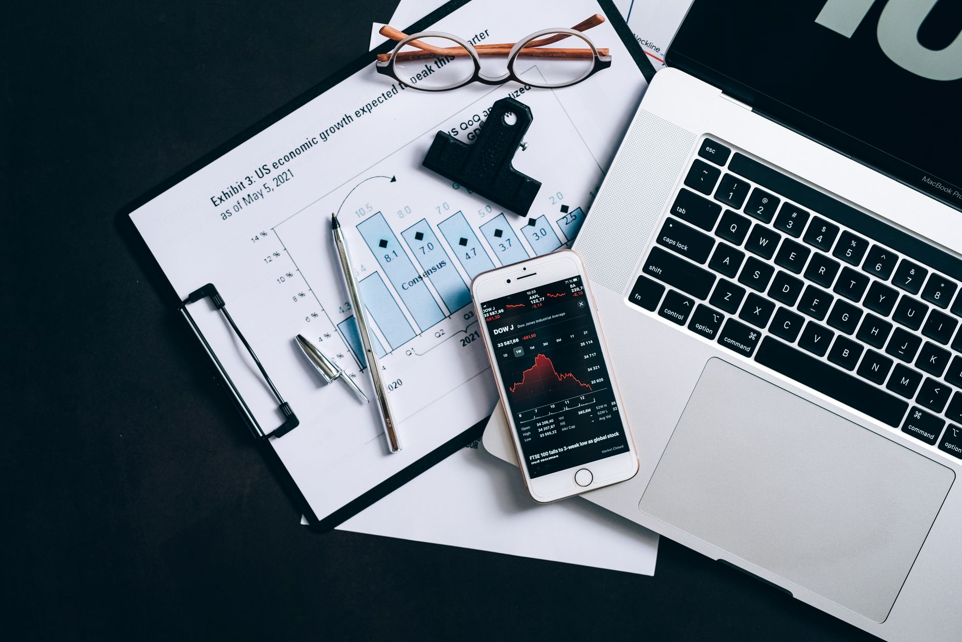 Top view of financial documents, laptop, and smartphone displaying stock market data.