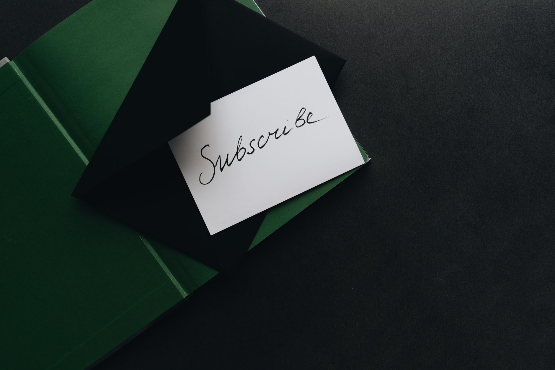 A minimalist image of a 'Subscribe' card in a green envelope on a dark background.