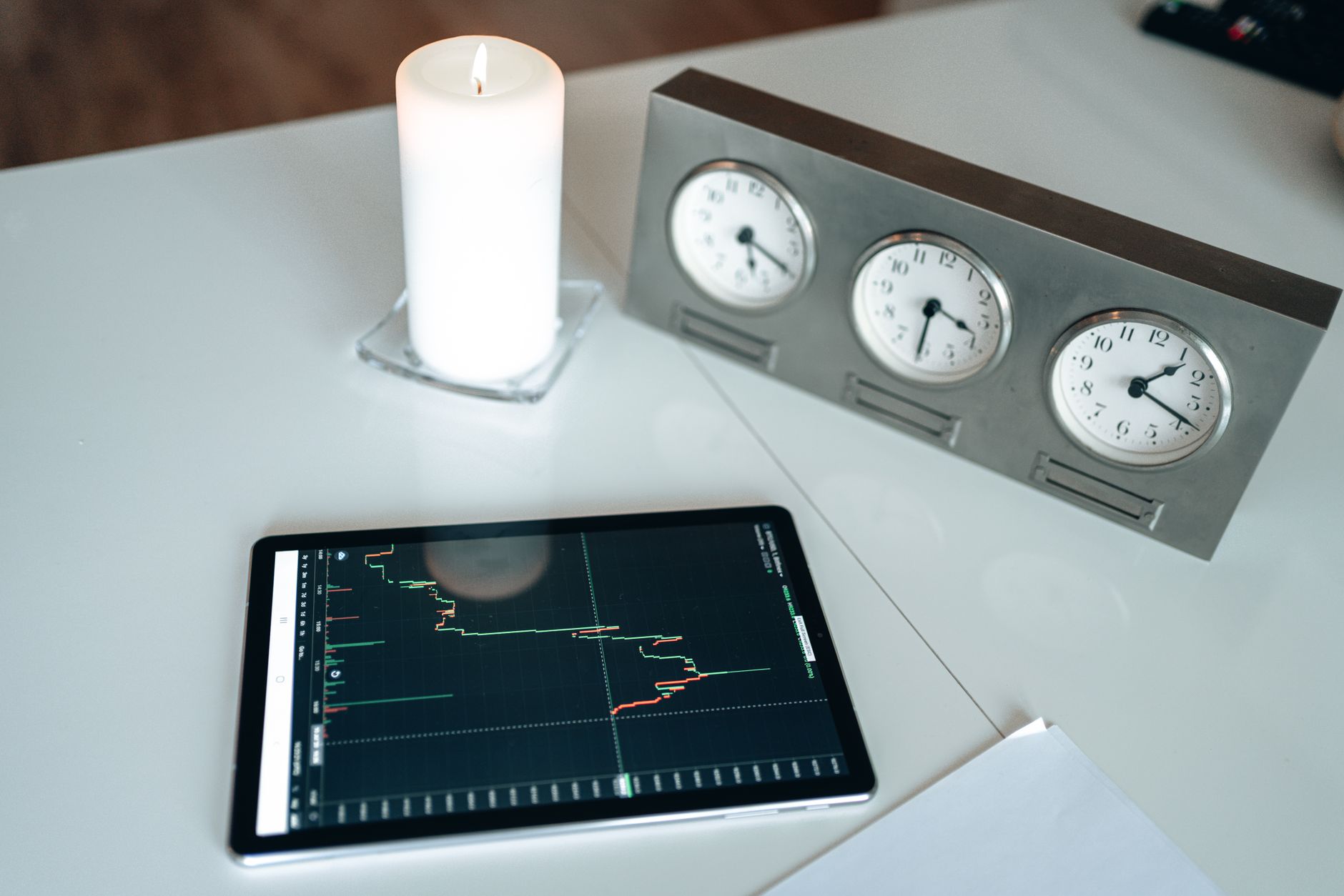Tablet displaying stock market data on a desk with a candle and world clocks, symbolizing global trading.