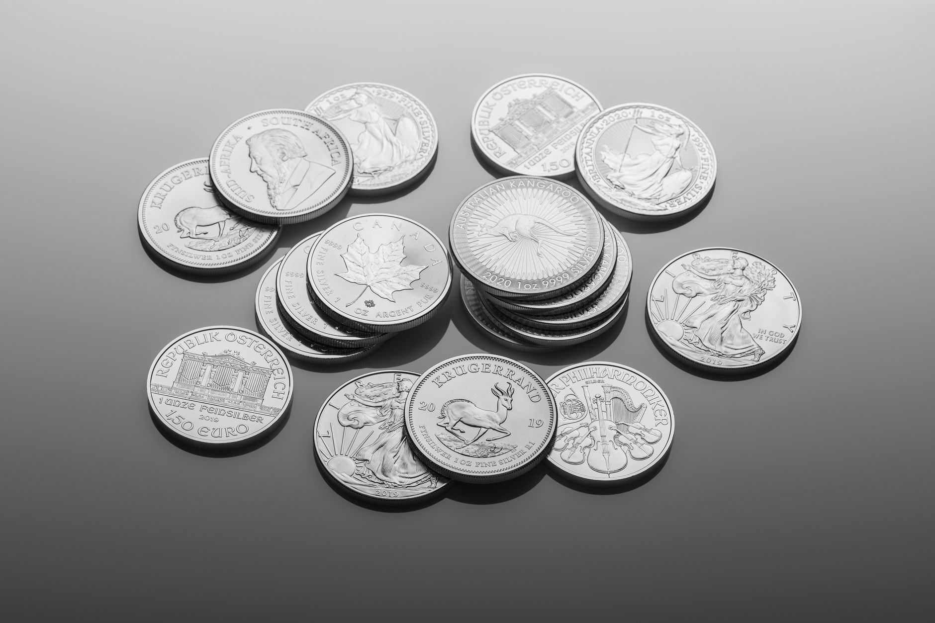 A close-up of various silver bullion coins, showcasing intricate designs on a reflective surface.
